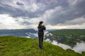 A girl stands on the edge of a cliff and takes pictures of a beautiful view.