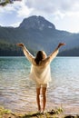 The girl stands with her back near a mountain lake in the background. Positive young woman traveling on a blue lake outdoors, Royalty Free Stock Photo