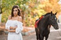 The girl stands with her back to the horse against the background of autumn foliage. Royalty Free Stock Photo