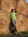 A girl stands near large bales of hay and looks out at the sunset