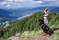 Girl with stands next to her dog of the Rottweiler breed on a peak with vegetation against the cloudy sky Royalty Free Stock Photo