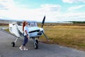 A girl stands next to a small plane on a field in the summer. Red-haired girl posing near the plane. Royalty Free Stock Photo