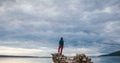 The girl stands on a pile of stones and looks at the sea