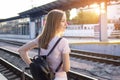 Girl stands on the platform of the station with a suitcase and waits for a train, a student travels, leaves for summer vacation, Royalty Free Stock Photo