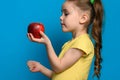 The girl stands in profile on a blue background and holds a large red apple in one hand. Royalty Free Stock Photo