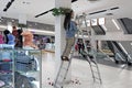 A girl stands on a stepladder in a store and decorates the post with garlands.