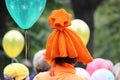 girl in a strange orange pumpkin-colored hat on the City Day holiday. In the background, colorful air balloons