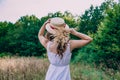 Girl in a straw hat with her back to the photographer. Girl in a white dress on a summer sunny day.