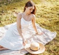 Girl with a straw hat in the spring in the park. Brunette with long hair sitting on a plaid on a background of summer nature. Royalty Free Stock Photo