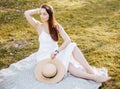 Girl with a straw hat in the spring in the park. Brunette with long hair sitting on a plaid on a background of summer nature. Royalty Free Stock Photo