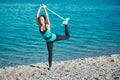 Girl stretching leg using rubber band. Coastline and calm ocean view. Sport and fitness idea. Healthy lifestyle concept