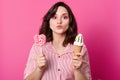 Girl in striped blouse, holding ice cream and lollipop, looking directly at camera, keeps lips rounded, has darkhair and bright Royalty Free Stock Photo