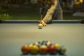 A girl in a striped dress holds a cue over a pool table with blue cloth and blurred billiard balls Royalty Free Stock Photo