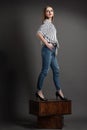 girl in a striped shirt and blue jeans stands on brown wooden crates, looks away, Royalty Free Stock Photo