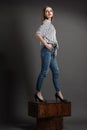 Girl in a striped shirt and blue jeans stands on brown wooden crates, looks away, gray background Royalty Free Stock Photo