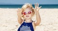 Girl in striped swimsuit on a white beach showing sandy hands