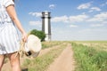 Girl in stripes overall with bunck of wheat and straw hat in right hand goes to black and white lighthouse y dirt road Royalty Free Stock Photo