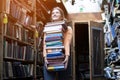 Girl student holds a large stack of books and carries a lot of literature in the library, she is preparing for study, the seller Royalty Free Stock Photo