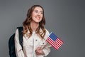 Girl student smiling, holding backpack and USA flag isolated on a dark grey background, copy space, student exchange concept