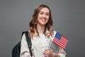 Girl student smiling, holding backpack and USA flag isolated on grey background, copy space, student exchange concept. Portrait of