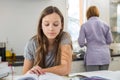 Girl studying at table with mother standing in background