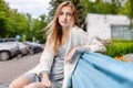 A girl in stylish clothes and beautiful looks is sitting on a blue bench in a summer park.