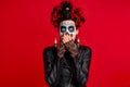 Girl with sugar skull makeup with a wreath of flowers on her head and skull, wearth black gloves close her opened shocked mouth