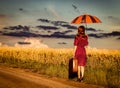 Girl with suitcase and umbrella waking on road Royalty Free Stock Photo