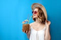 Girl in summer clothes drinks a tropical pineapple cocktail and smiles on a blue isolated background, a woman with an exotic drink