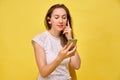 A girl in summer clothes stands on a yellow background and listens to music in wireless headphones through a smartphone switching