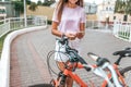 Girl summer stands bicycle, activates application buying rental bicycle in parking lot, in hands of phone. Online