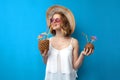 Girl in a sun hat and glasses drinks tropical cocktails made of pineapple and coconut on a blue isolated background, a woman with Royalty Free Stock Photo