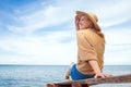 Girl in sun hat sits on pier at the sea and looks at the horizon, travel and freedom concept