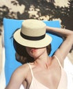 The girl sunbathes in a lounge chair near the pool, covering her face with a hat Royalty Free Stock Photo