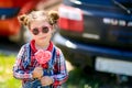 Girl in sunglasses and candy on a stick in her hands on the background of cars Royalty Free Stock Photo