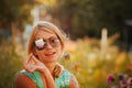 Girl in sunglasses is holding a flower in front of her face, closing one eye. The concept of Russian beauty, a gentle blonde with