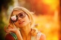 Girl in sunglasses is holding a flower in front of her face, closing one eye. The concept of Russian beauty, a gentle blonde with