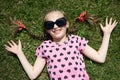 Girl in sunglasses lie on green grass, dressed in pink clothes with hearts, bright sun, summer outdoor, top view