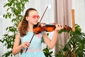 A girl in sunglasses plays the violin at home among green plants Royalty Free Stock Photo