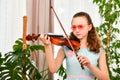 A girl in sunglasses plays the violin at home among green plants Royalty Free Stock Photo