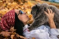 A girl in sunglasses and a red bandana on her head lies on yellow fallen maple leaves and holds a British cat in her arms. Royalty Free Stock Photo