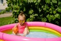 Girl splashes in a small inflatable round swimming pool next to the house Royalty Free Stock Photo