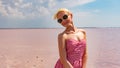 A girl in sunglasses stands against a sea of pink salt water, in a red dress Royalty Free Stock Photo