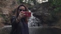 Girl in sunglasses taking a selfie against the backdrop of a small waterfall