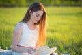 A girl on a sunny day sits on a plaid and reads a book in a field with green fresh grass Royalty Free Stock Photo