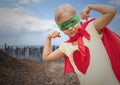 Girl in superhero costume flexing her arms against cityscape