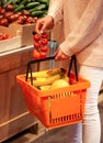 Girl in the supermarket holds a basket full of fruits and want to add a branch of cherry tomatoes Royalty Free Stock Photo