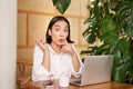 Girl with surprised face, pitching an idea, pointing left, sitting with laptop in cafe and drinking coffee Royalty Free Stock Photo