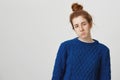 Girl is suspicious, having doubts. Portrait of cute ginger girl in bun and winter sweater squinting at camera and