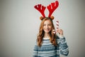 Girl in a sweater with red horns smiles, holding a Christmas lollipop in her hand. She will be happy to decorate the Royalty Free Stock Photo